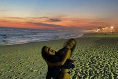 a woman is hugging her friend on the beach at sunset or sunrise, with people in the background