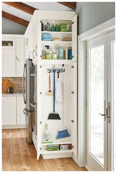 an organized kitchen with white cabinets and wood flooring, including brooms and cleaning supplies