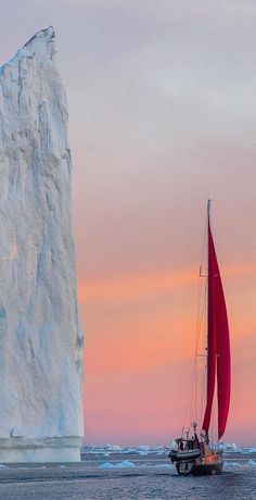 a sailboat in front of an iceberg at sunset