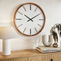 a large clock mounted to the side of a wall next to a lamp on a dresser