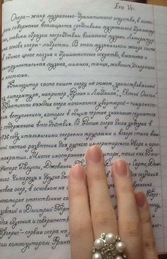 a woman's hand holding onto an open book with writing on the pages and pearls