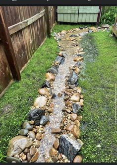 a small stream running through a yard next to a wooden fence and green grass area