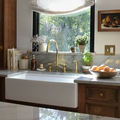 a white kitchen sink sitting under a window next to a bowl of fruit on top of a counter