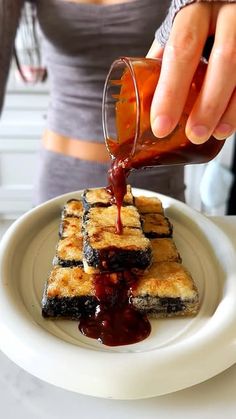 a person pouring syrup onto some food on a plate