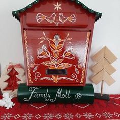 a red and green mailbox sitting on top of a table next to christmas trees