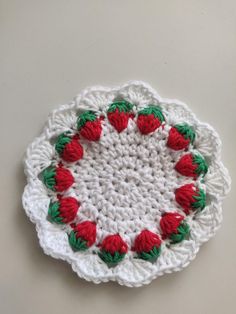 a crocheted dishcloth with red and green flowers on the center, sitting on a white surface