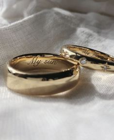 two gold wedding rings with the words my sun written on them sitting on a white cloth