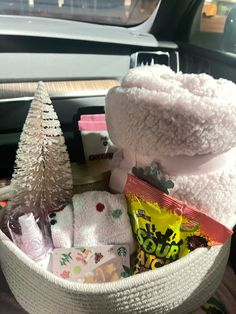 a white basket filled with various items next to a christmas tree in the back of a car