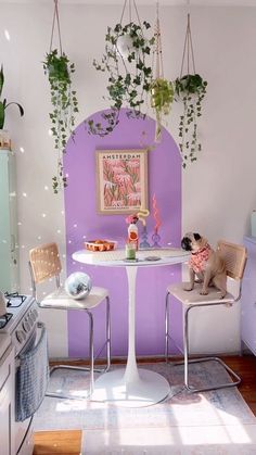 two chairs and a table in a room with plants hanging on the wall above them