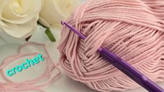 a ball of pink yarn with a crochet hook next to it and two white roses