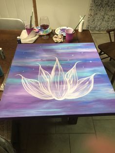 a table with a painting on it that has a white flower in the middle and purple background