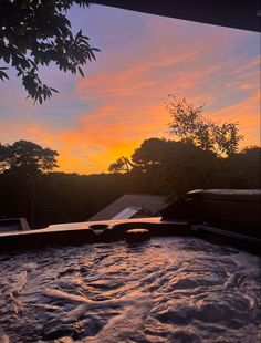 a hot tub with the sun setting in the background and some trees around it,