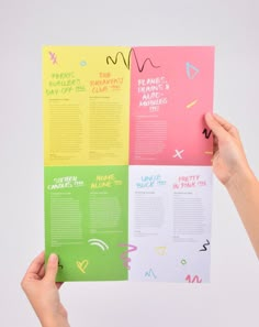 two hands holding up an open brochure with different colored papers on it and writing