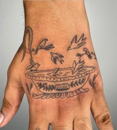 a person's hand with tattoos on it and birds flying around the bowl in the middle