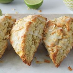 three pieces of cake sitting on top of a cutting board next to limes and a cup