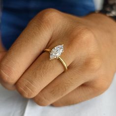 a woman's hand wearing a gold ring with a pear shaped diamond