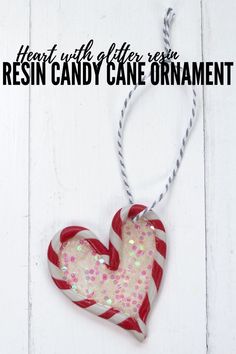 a red and white heart shaped candy cane ornament hanging from a string on a white wooden background