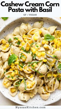 a white bowl filled with pasta and corn on top of a table next to a fork