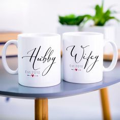 two white coffee mugs with the names hubby and wife on them sitting on a table