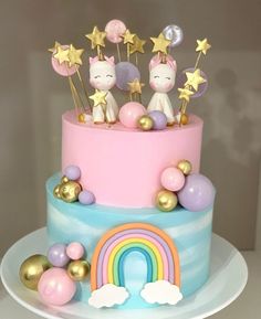 a pink and blue cake with gold stars, unicorn figurines and rainbow decorations