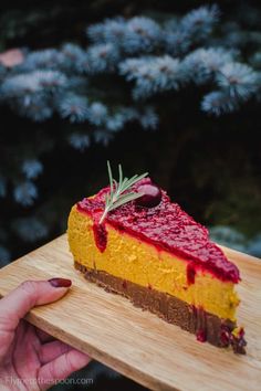 a person holding a piece of cheesecake on a wooden cutting board in front of some trees