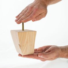 two hands holding a small wooden object with one hand and the other hand reaching for it