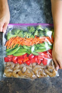 a person holding a plastic bag full of vegetables and shrimp in front of their feet