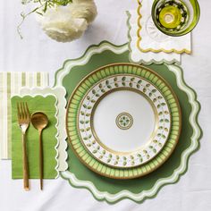 a place setting with green and white plates, napkins, silverware and flowers