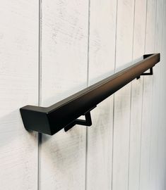 a metal shelf mounted to the side of a white wall with wood planks behind it