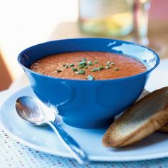 a blue bowl filled with soup on top of a white plate next to some bread