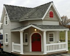 a small white house with a red door and porch on train tracks in front of it