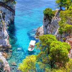 a boat is floating in the clear blue water near some rocks and trees on the shore