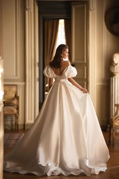 a woman in a white wedding dress standing on a wooden floor with her back to the camera