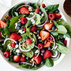 a white bowl filled with spinach, strawberries and blueberries on top of a table