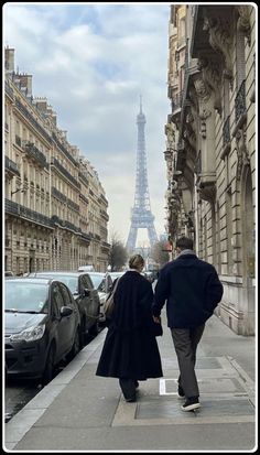 a man and woman walking down the sidewalk in front of the eiffel tower