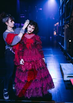 two women in red and purple dresses on stage with one holding the other's hair