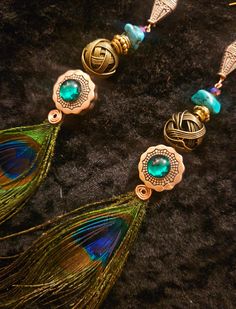 peacock feathers are attached to some gold and green beads on a black surface with other jewelry items in the background