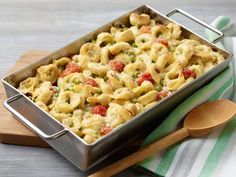 a casserole dish with pasta and vegetables in it on a wooden board next to a spoon