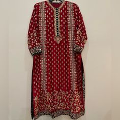 a red and gold dress hanging on a hanger in front of a white wall