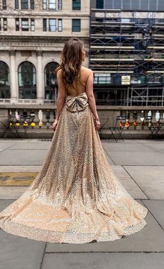 a woman standing on the sidewalk wearing a dress with an open back and gold sequins