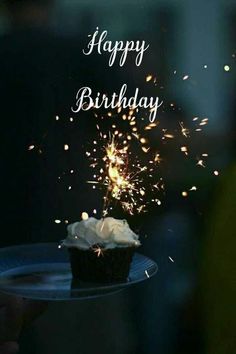 a cupcake on a plate with sparklers in the background that says happy birthday