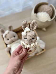 a hand holding a small crocheted bunny in front of two other stuffed animals