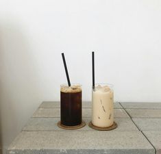 two drinks sitting next to each other on top of a stone block counter with black straws