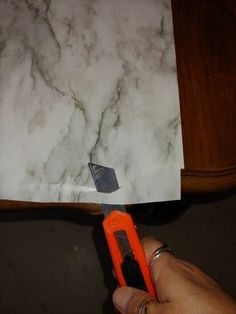 a person holding an orange handled tool in front of a piece of paper on top of a table