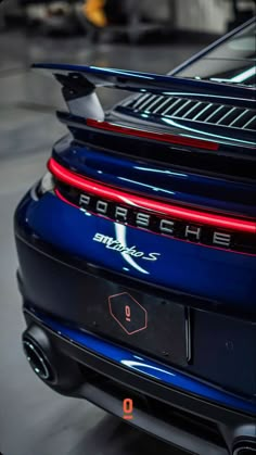 the rear end of a blue porsche sports car with its hood up and tail lights on