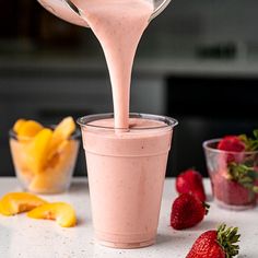 a person pouring pink smoothie into a cup with strawberries