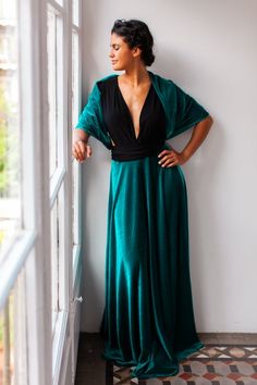 a woman standing next to a window in a long green dress and black top with her hands on her hips