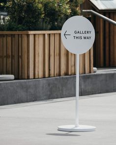 an open sign sitting on top of a cement ground next to a wooden fence and bushes