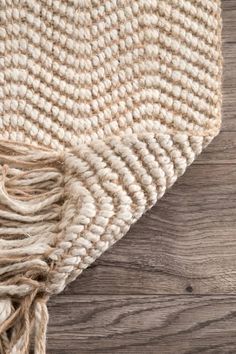 an area rug on top of a wooden floor with white and beige accents, including fringes