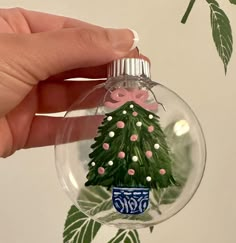 a hand is holding a glass ornament with a christmas tree on the inside